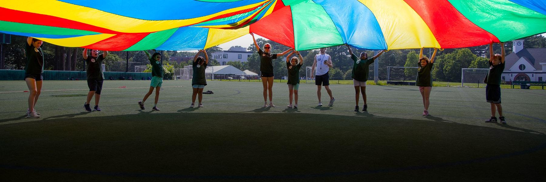 students in long line holding colorful rainbow banner above heads