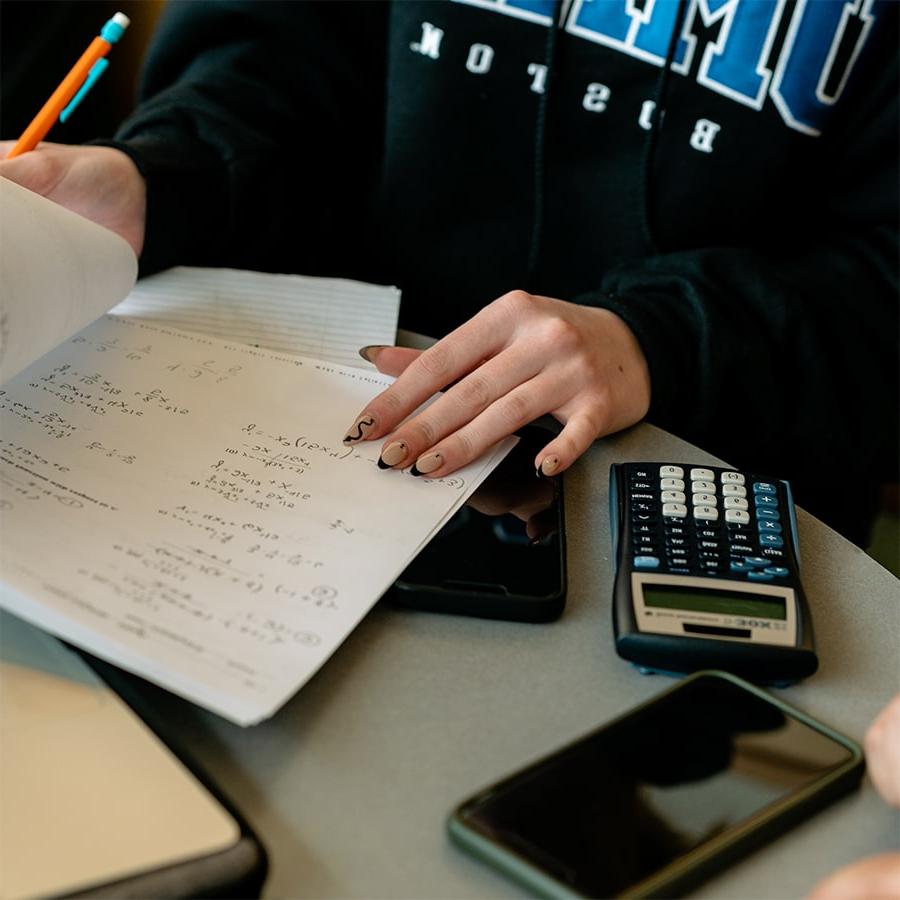 close up of hand with painted fingernails with calculator and notes on paper